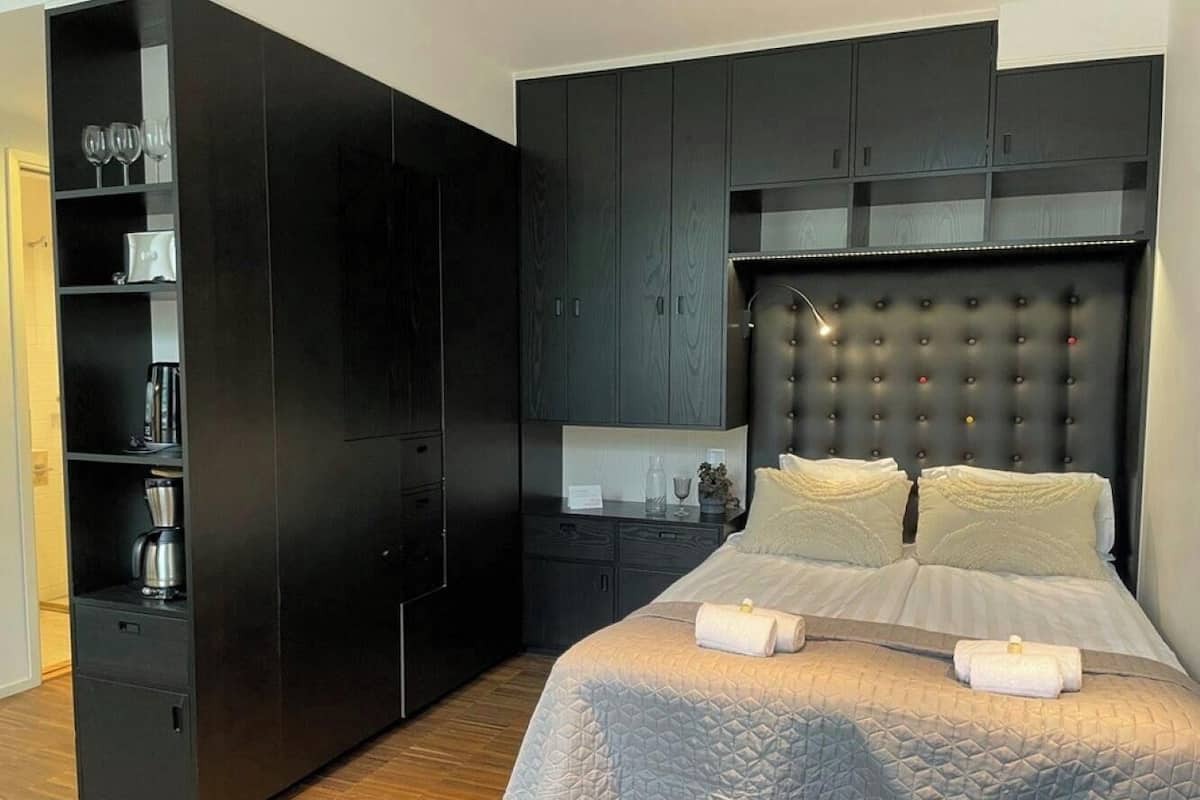 Une chambre avec un grand lit, une armoire en bois foncé et une étagère intégrée où sont rangés des verres et une machine à café.