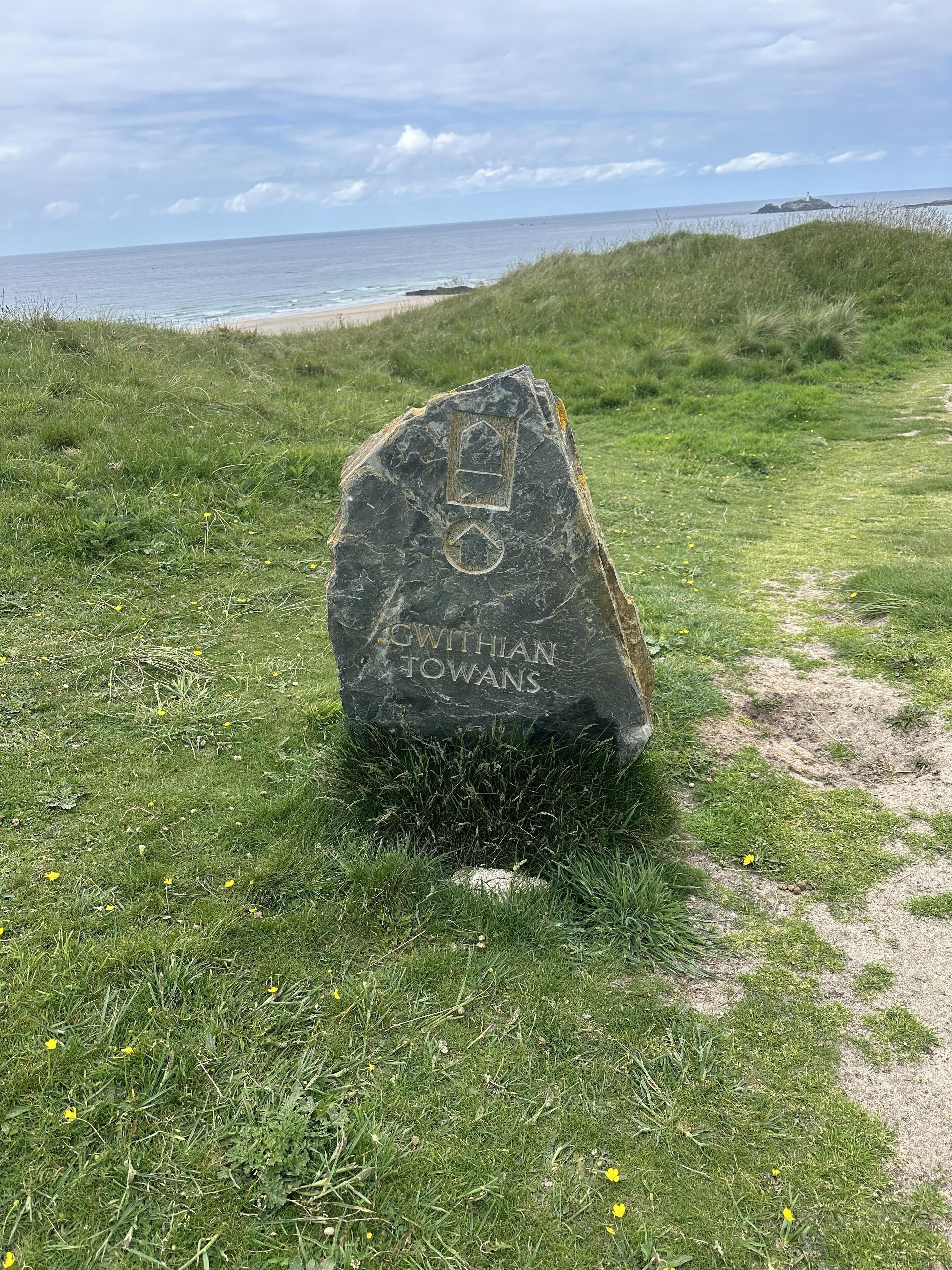 Un monument de pierre portant des inscriptions, situé dans un espace verdoyant près d’une plage.
