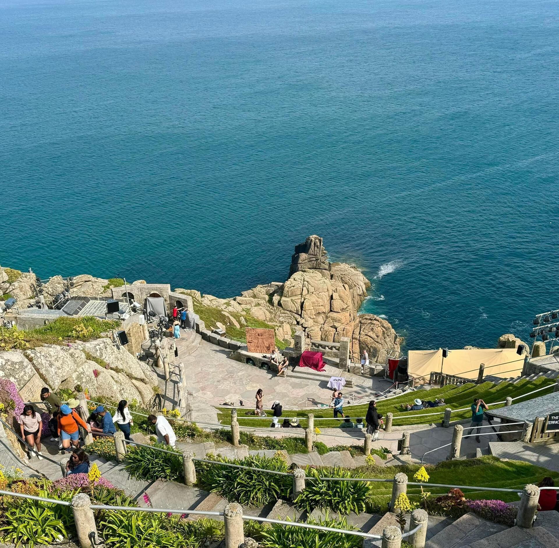 Un mirador costero con un promontorio rocoso, escaleras que bajan al mar y una zona pavimentada con vegetación.