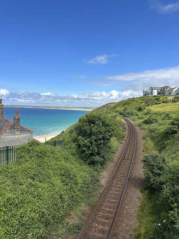 A railway track curving along a coastal landscape with a building on the left and a residential area on the right.