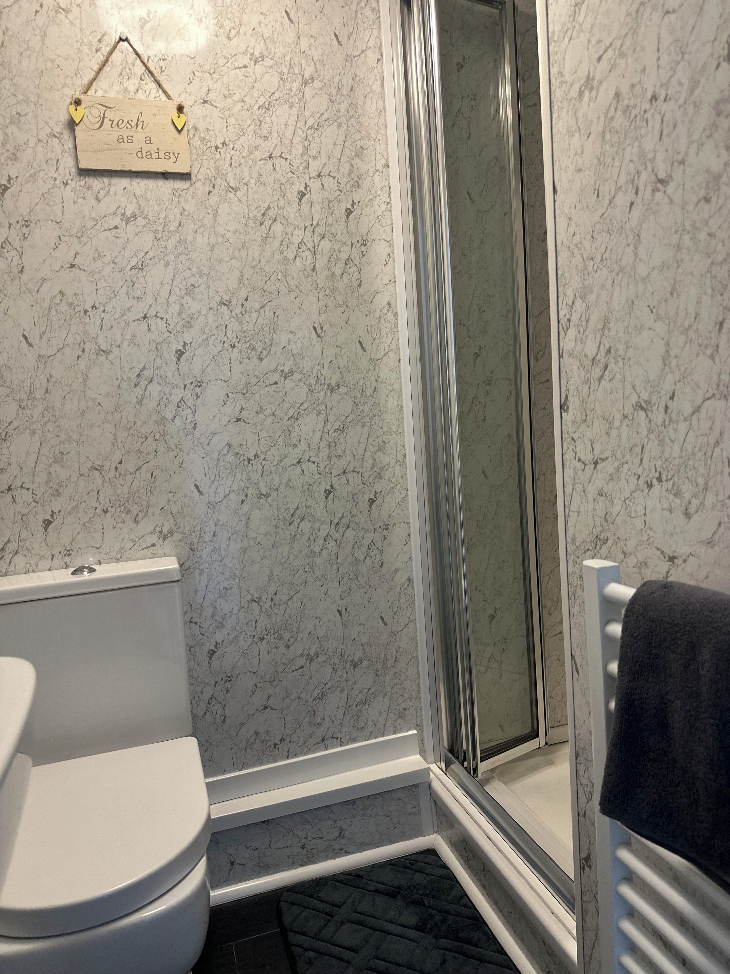 Une salle de bain avec des toilettes, une douche dotée d’une porte en verre et un mur en marbre.