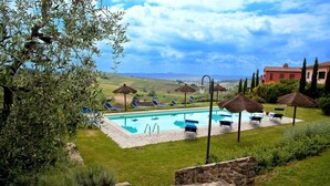 Zona de piscina con sillones de descanso y sombrillas, rodeada de vegetación y vistas al campo.