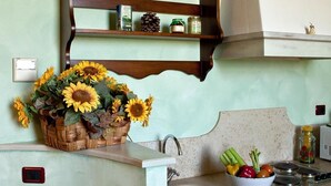 Una cocina con un estante de madera que sostiene frascos y una cesta de girasoles.