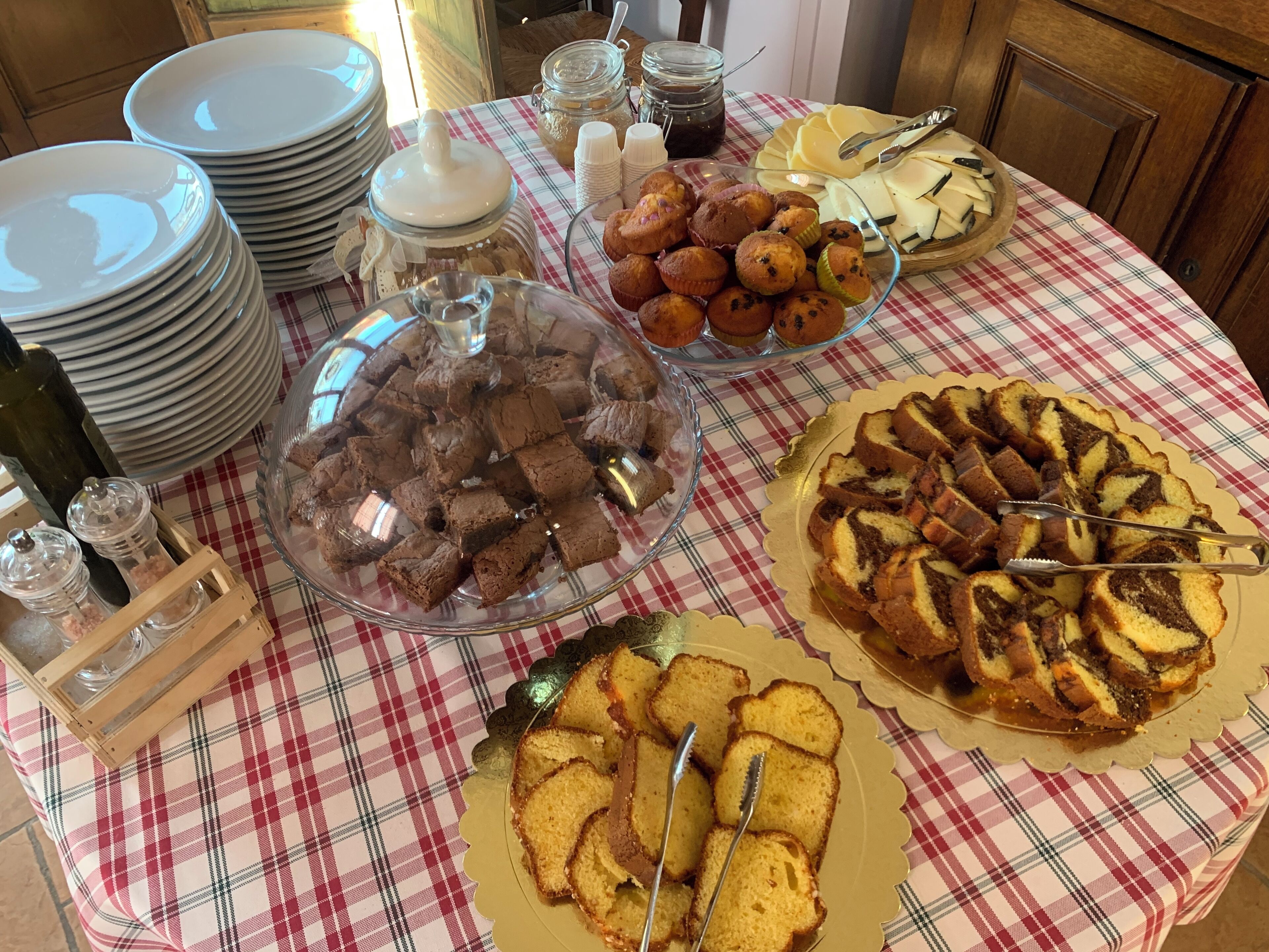 Une table sur laquelle sont disposés divers aliments, notamment des brownies, des muffins et un gâteau, avec des assiettes empilées à proximité.