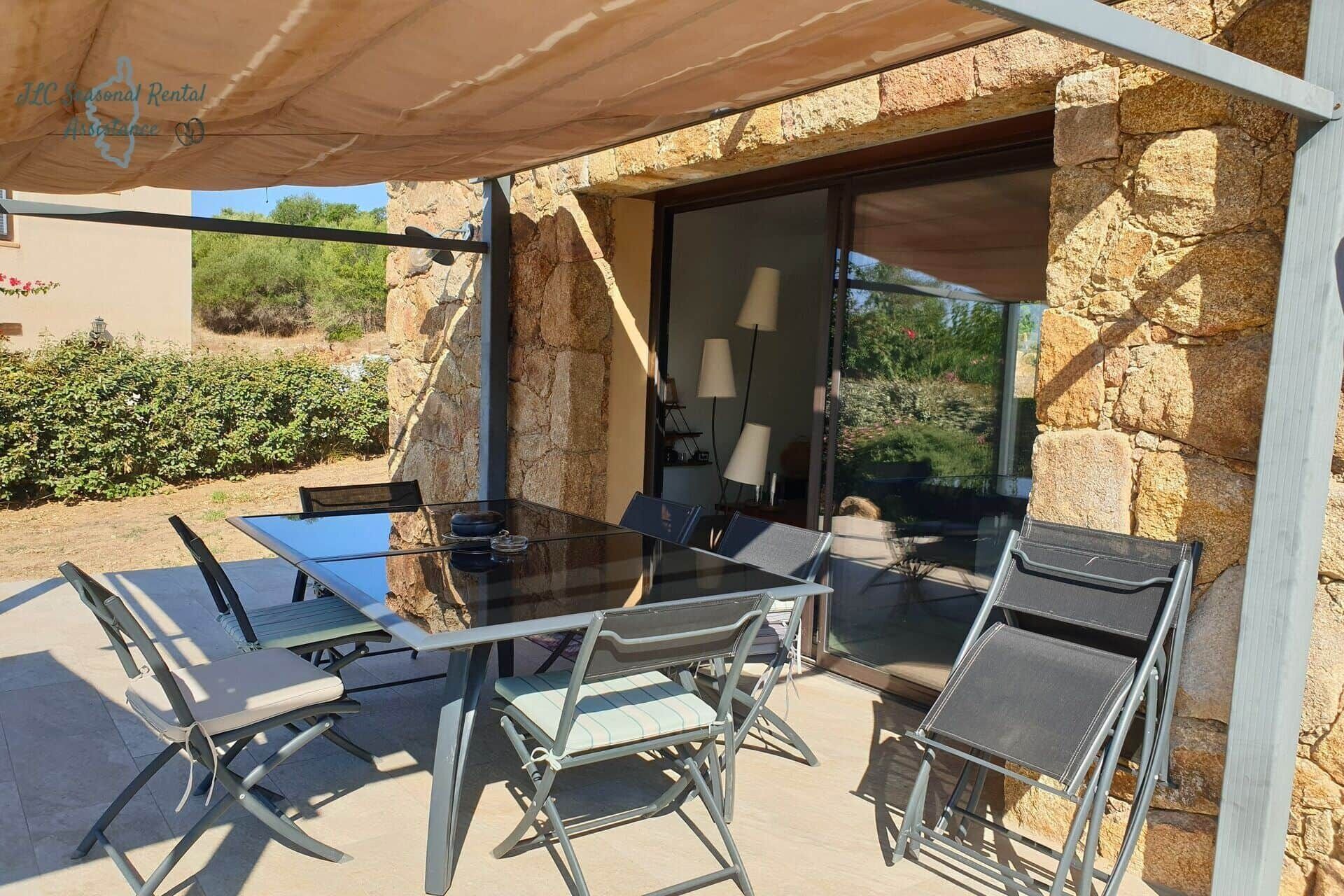An outdoor patio with a glass table and chairs, a stone wall, and a view of the surrounding landscape.