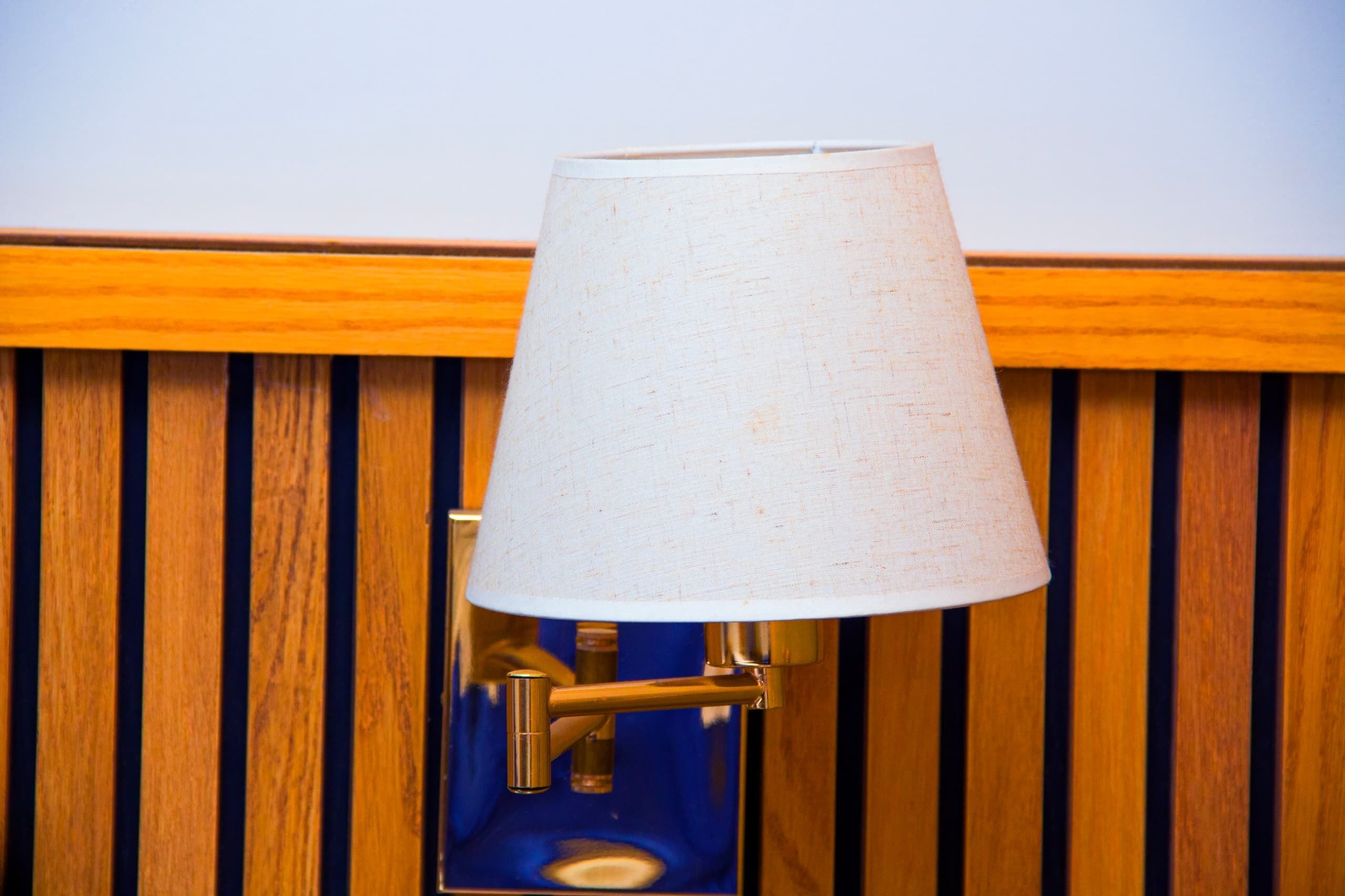 A lamp with a white shade mounted on a wooden wall with vertical slats.