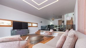 Un salon moderne comprenant un canapé, des fauteuils, une table basse et un téléviseur. Un escalier mène à un niveau supérieur.