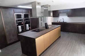 Eine moderne Küche mit einer zentralen Kochinsel, eingebauten Backöfen und einer dunklen Holzoptik.