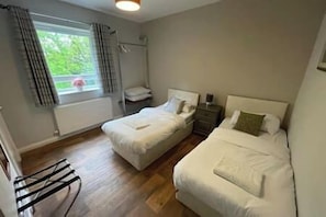 Ein Schlafzimmer mit zwei Einzelbetten, einem Fenster mit Vorhängen, einem Heizkörper und einem kleinen Tisch.