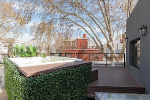 Terraza en la azotea con jacuzzi, cubierta de madera y vistas a un edificio de ladrillo rojo y árboles.