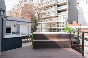 An outdoor terrace with a wooden deck, a seating area, and a view of a modern building with balconies.