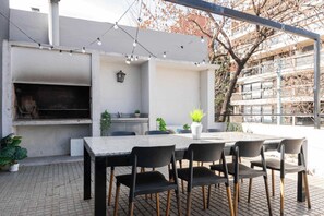 Une terrasse extérieure équipée d’un barbecue, de sièges et de guirlandes lumineuses.
