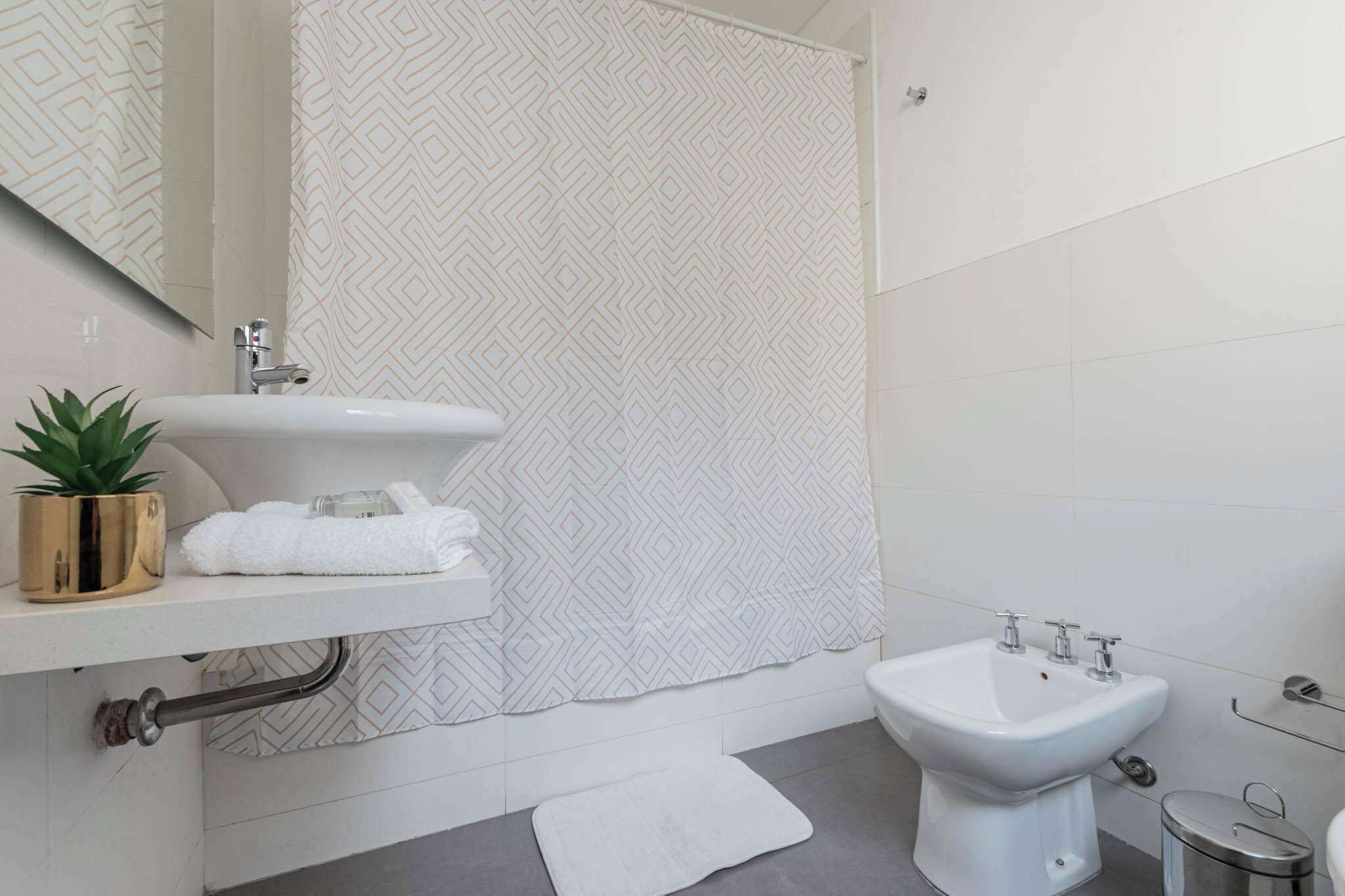 Une salle de bain moderne avec un lavabo blanc, un bidet, un porte-serviettes et un rideau de douche à motifs géométriques.