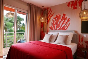 Un dormitorio con una cama grande, un balcón con vistas a palmeras y una pared con un diseño que recuerda al coral.