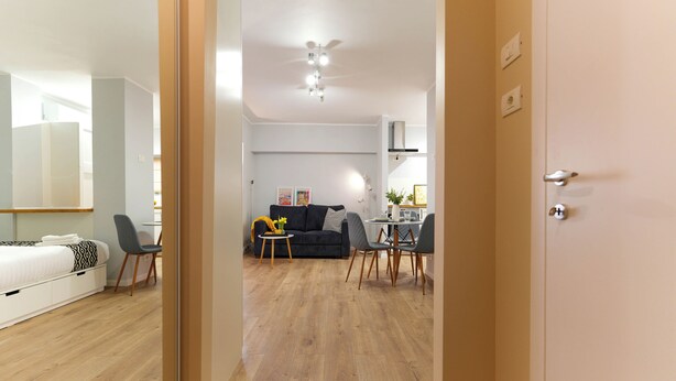 A modern apartment with a wooden floor, a living area with a sofa and chairs, a dining table, and a kitchen area. - Andreea (Bucharest)