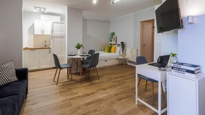 A compact living space with a kitchenette, a dining area, a sofa, a TV, and a desk with a computer and books. - Andreea (Bucharest)