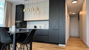 A modern kitchen with dark cabinetry, a wooden floor, and pendant lighting. - Joy City Stay Nord One N2-52 (Timișoara)