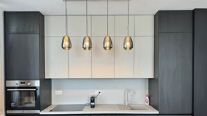 A modern kitchen with dark cabinetry, a built-in oven, a sink, and pendant lighting. - Joy City Stay Nord One N2-52 (Timișoara)