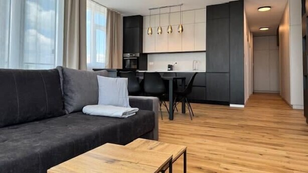 A modern living room with a dark grey sofa, a wooden coffee table, and a dining area with a black table and chairs. - Joy City Stay Nord One N2-52 (Timișoara)