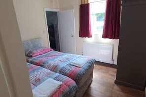 A bedroom with two beds, a radiator, and a window with red curtains. - 17 Bedroom Huge Holiday Home.  When SIZE is important. (Bontnewydd)