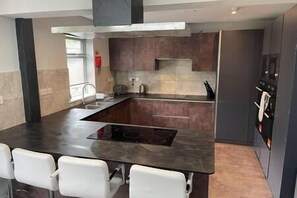A modern kitchen with a central island, dark cabinetry, and a stainless steel range hood. - 17 Bedroom Huge Holiday Home.  When SIZE is important. (Bontnewydd)