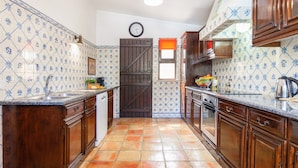 A kitchen with wooden cabinets, a tiled backsplash, a clock, and a window with a view. - Villa Dreams (Albufeira)