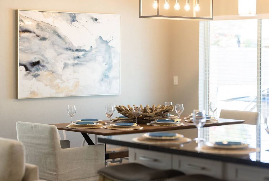 A dining area with a wooden table set for six, a large abstract painting on the wall, and a modern chandelier.