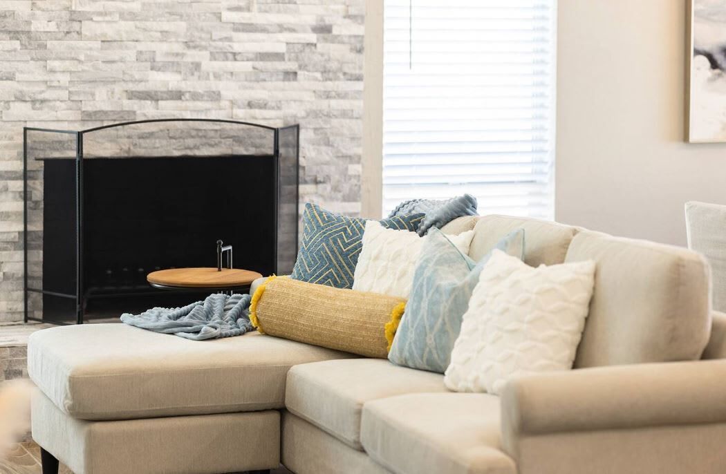 A modern living room with a sectional sofa, a black entertainment unit, and a stone wall.