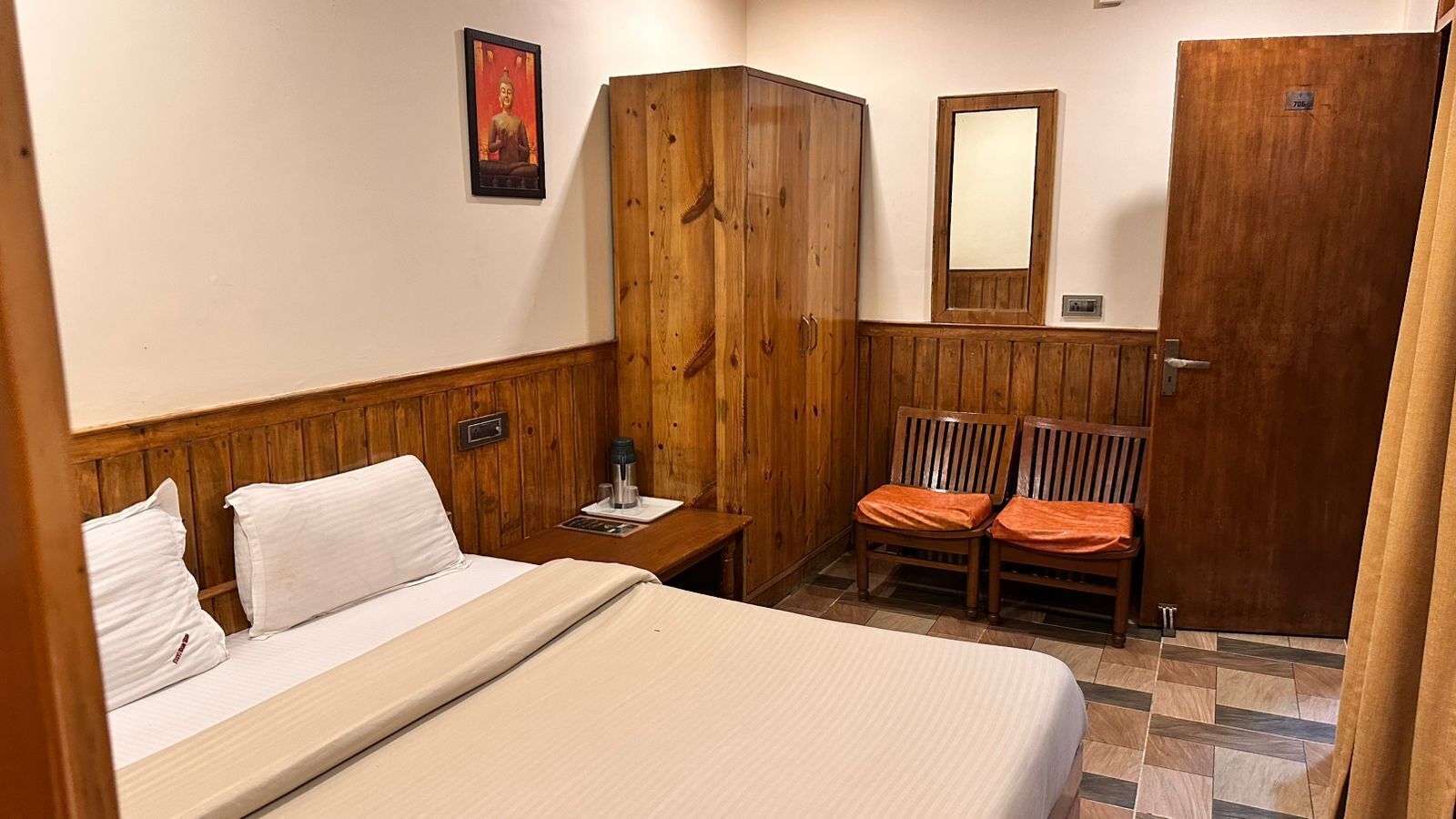 Una habitación de hotel con cama, armario de madera, dos sillas, una mesita y un espejo.