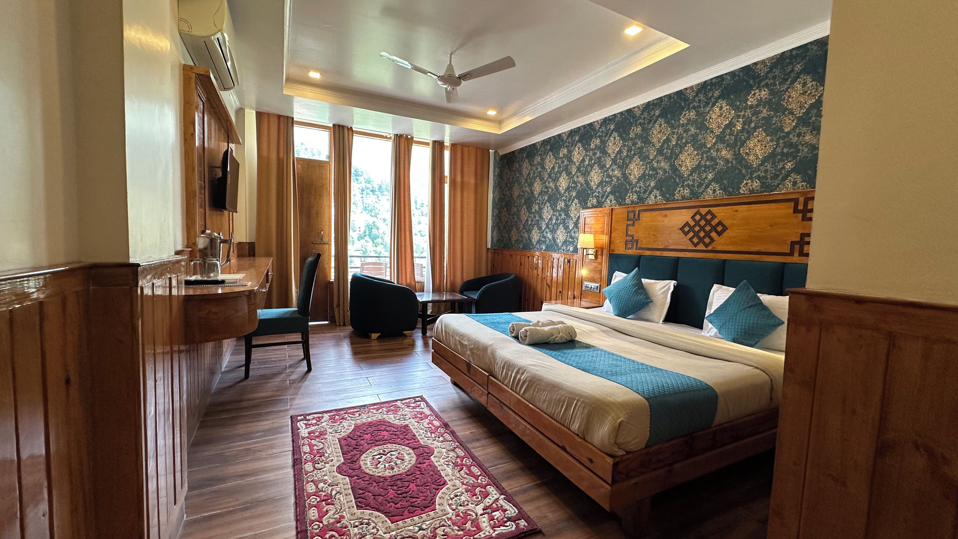 A hotel room with a bed, desk, chair, and a large window.