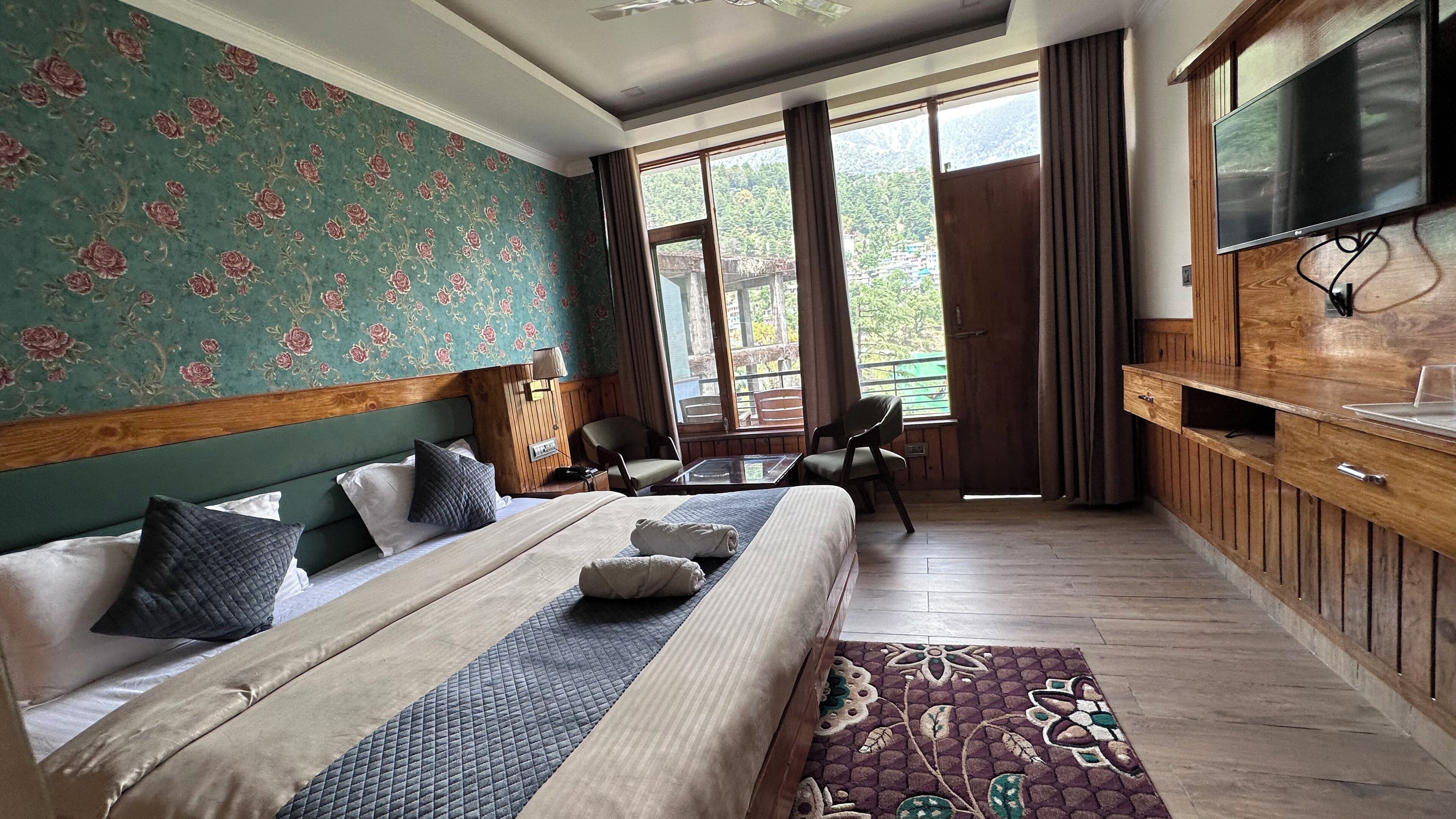 Habitación de hotel con cama, escritorio, televisor y vistas al exterior.
