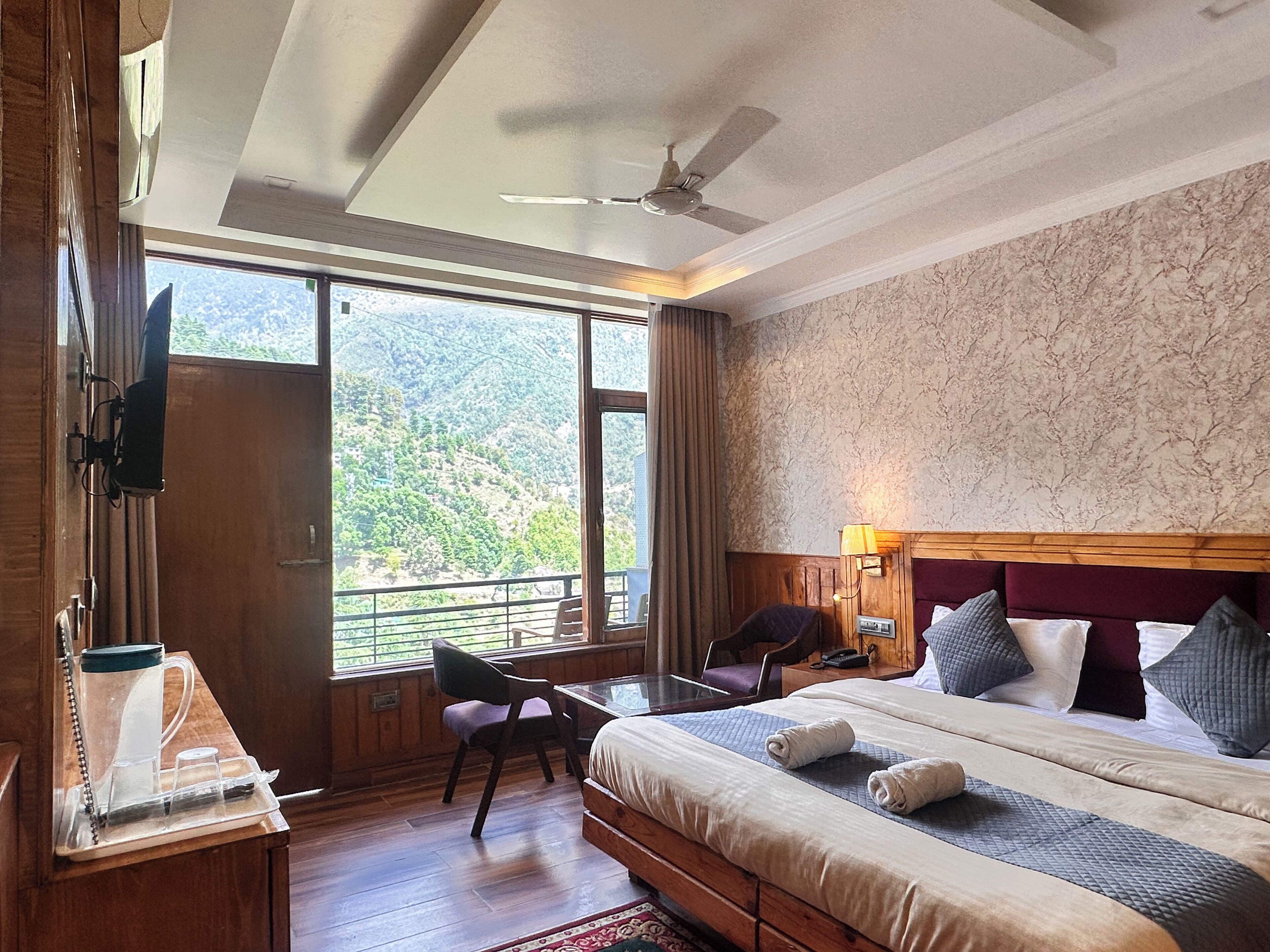 Habitación de hotel con cama, escritorio con silla, televisor y vistas al exterior.