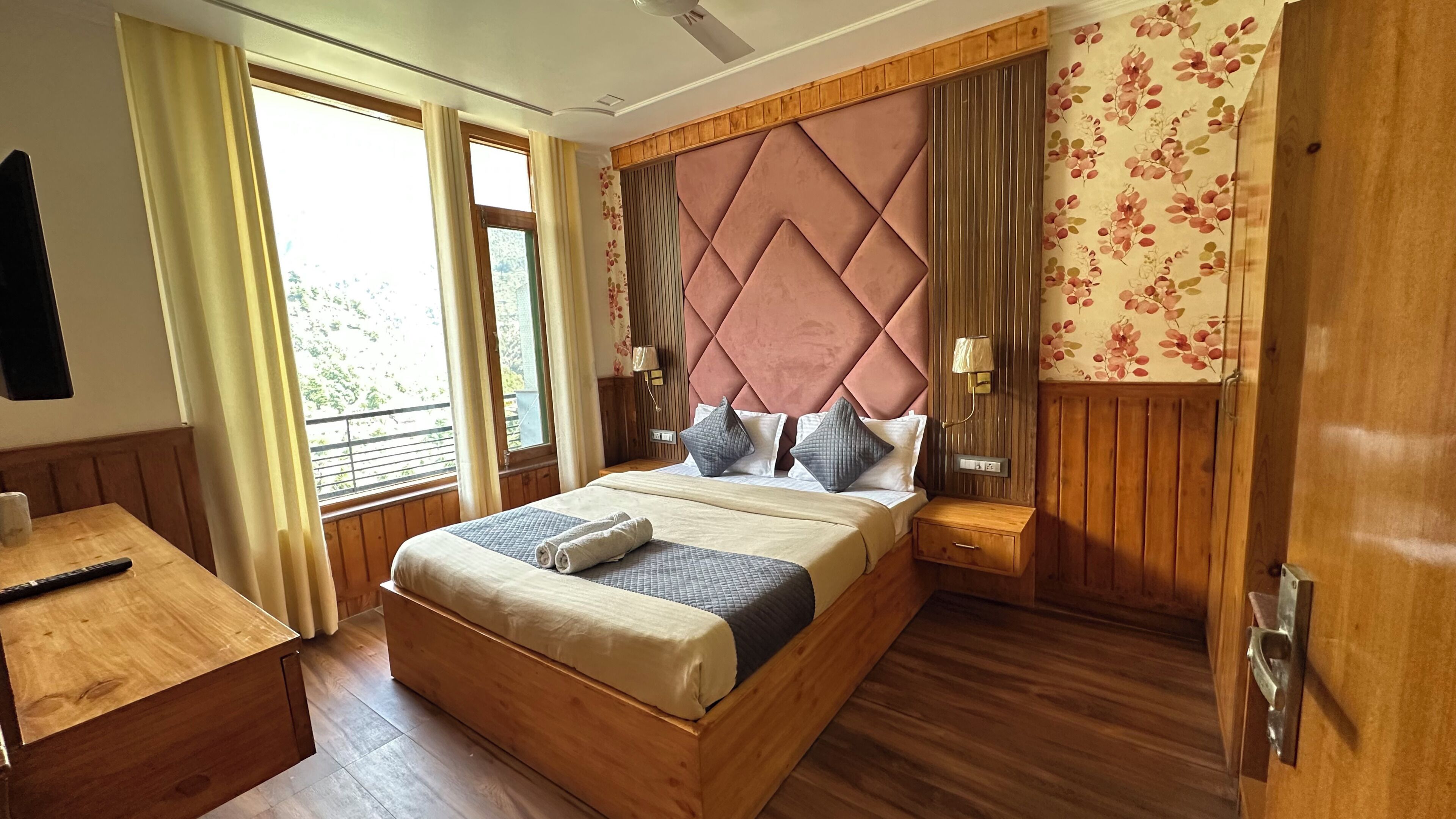 A wooden-framed bed with a tufted headboard, bedside lamps, and a view of greenery outside.