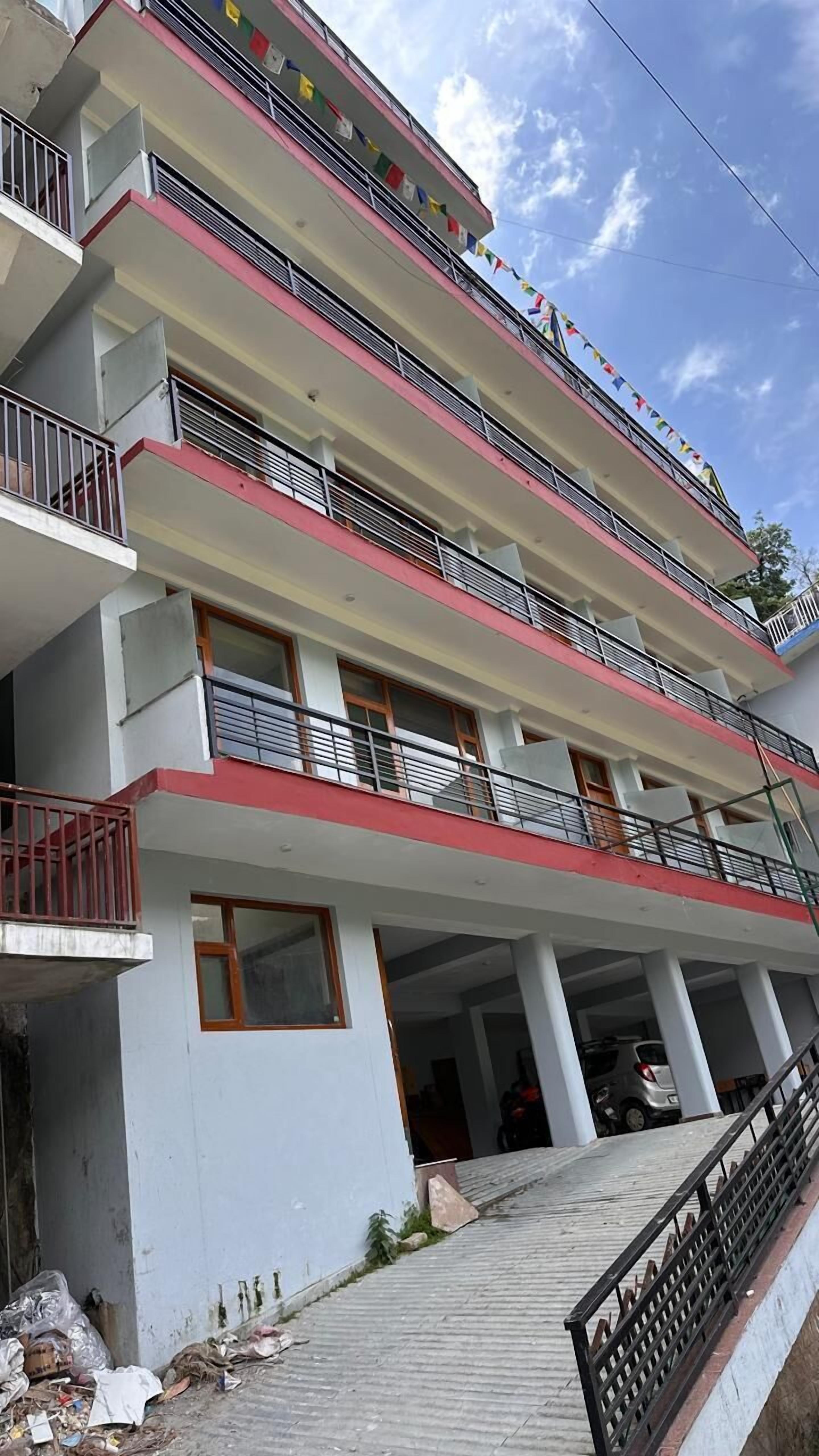A multi-story building with balconies, a covered parking area, and a staircase leading to the entrance.