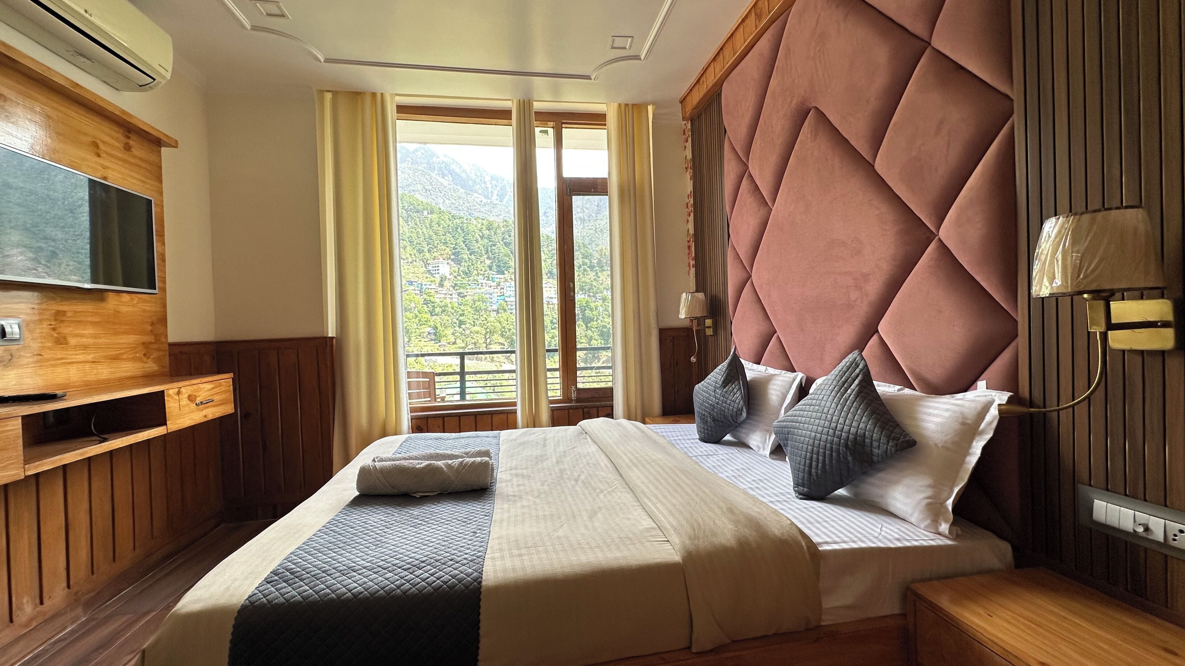 A bedroom with a large bed, wooden paneling, a television, and a view of greenery.
