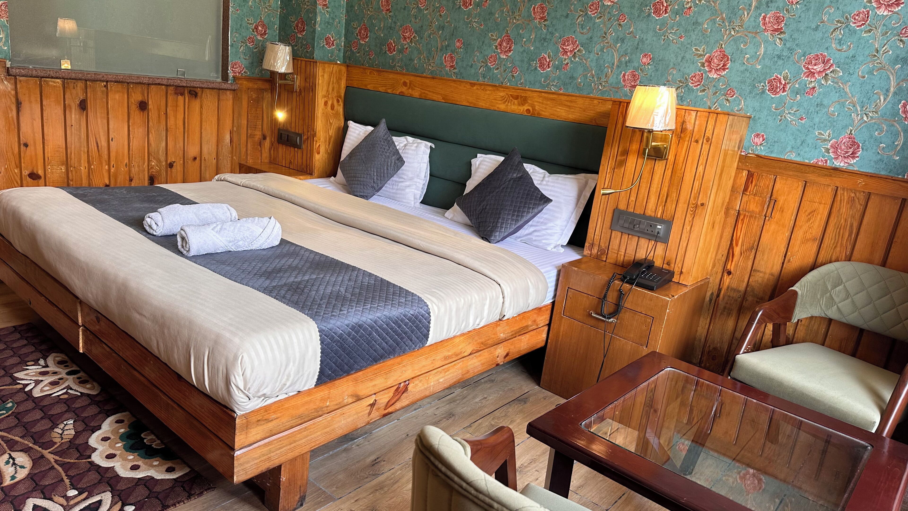 A wooden bed with a headboard, a bedside table with a lamp, a chair, and a small table.