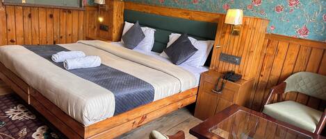 A wooden bed with a headboard, a bedside table with a lamp, a chair, and a small table.