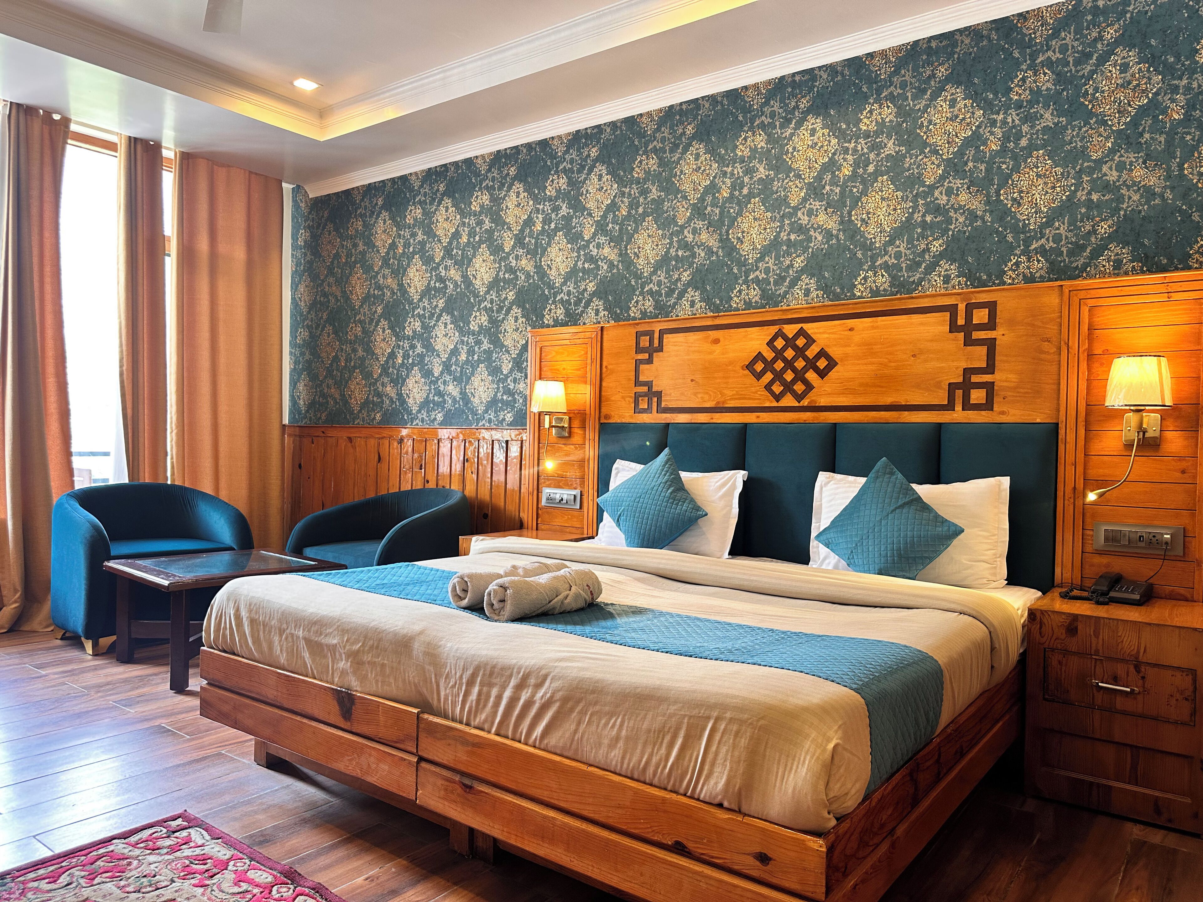 A bedroom with a wooden bed, two chairs, a nightstand, and a patterned wall.