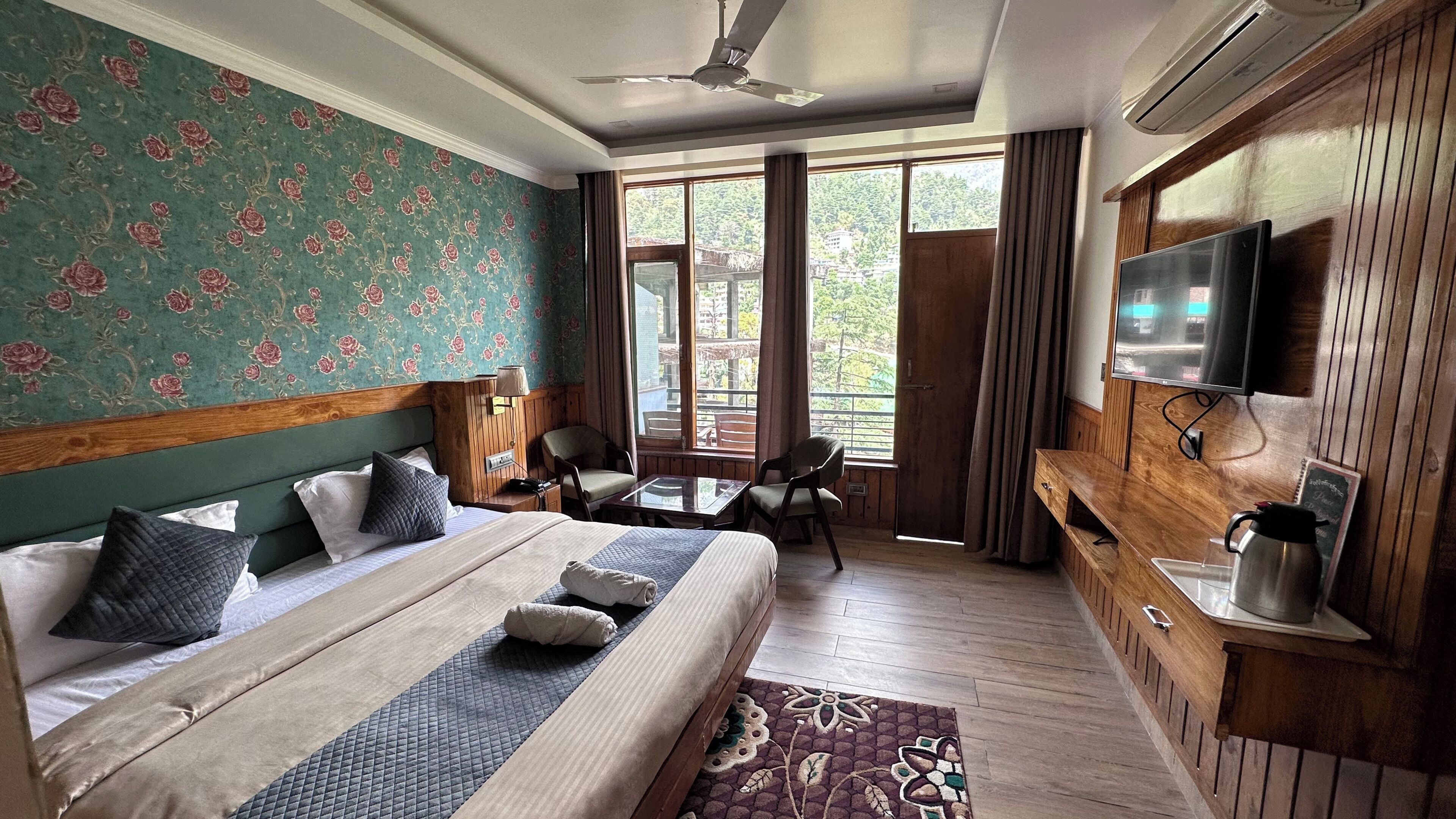 Ein Hotelzimmer mit Bett, Schreibtisch, Stuhl, Fernseher und einem Fenster mit Blick auf Grünflächen.