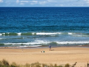 Een strand met een persoon die aan het vissen is, een hengel en een groene tas in het zand.