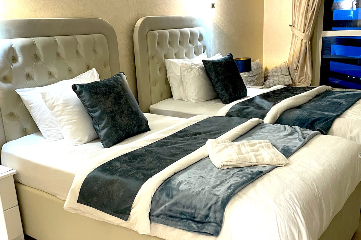 Une chambre d’hôtel avec deux lits, chacun doté d’une tête de lit capitonnée, de draps blancs et de coussins décoratifs bleu foncé.