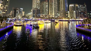 Un paisaje urbano nocturno con edificios altos iluminados y un río con barcos.