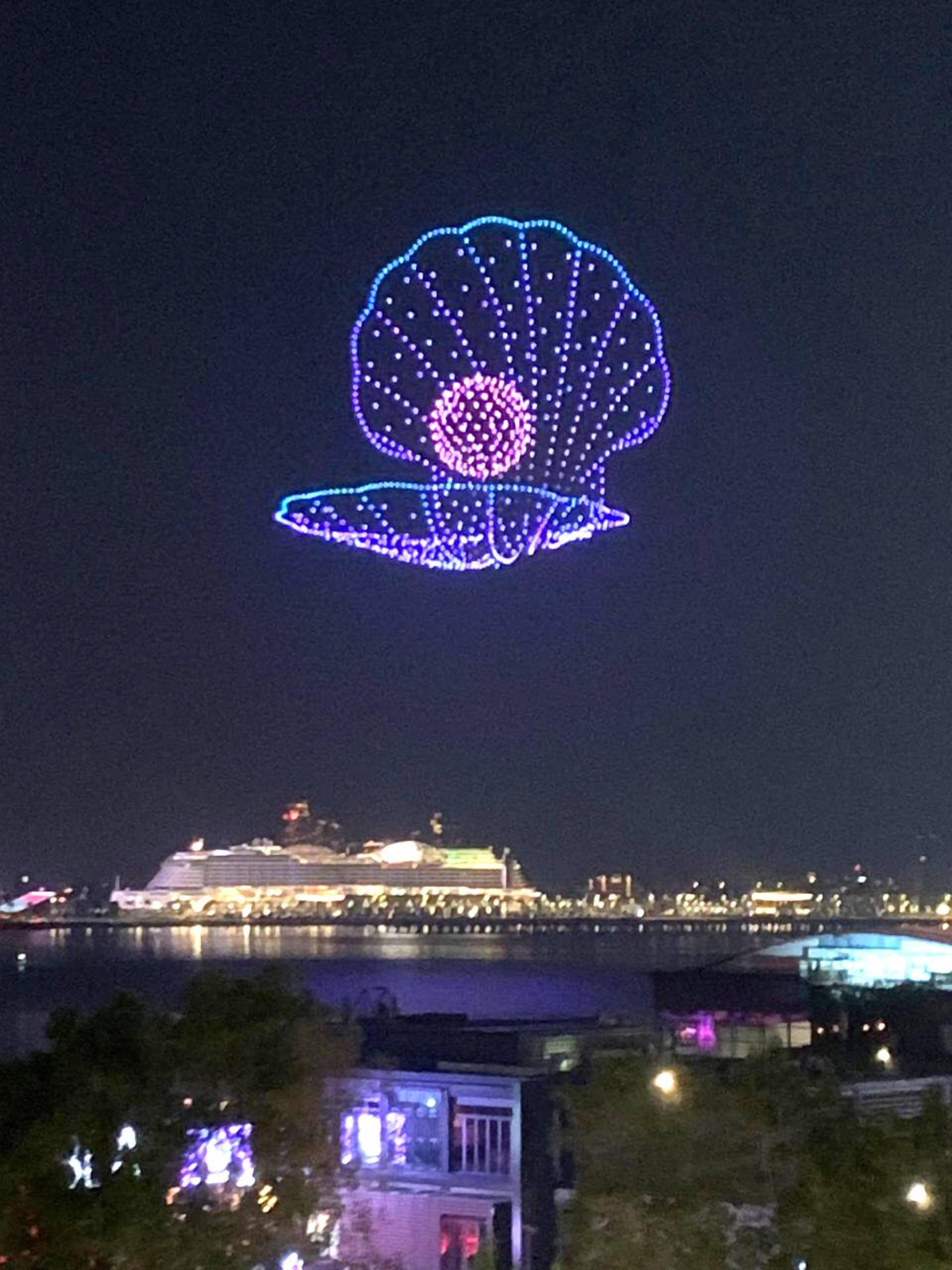 A large illuminated lotus flower structure at night, with a cityscape and a body of water in the background.