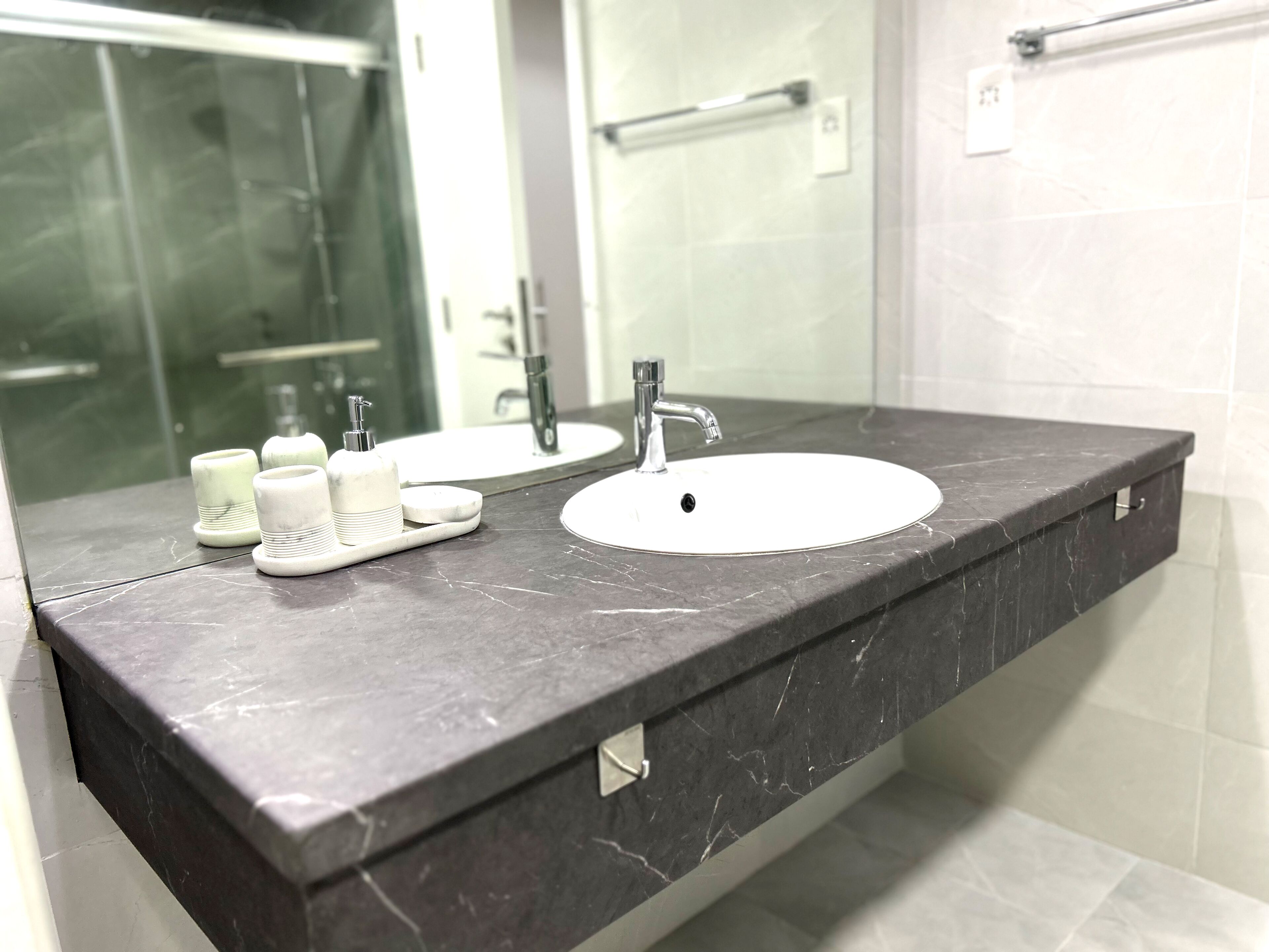 A modern bathroom with a dark marble countertop, a white sink, and a large mirror.