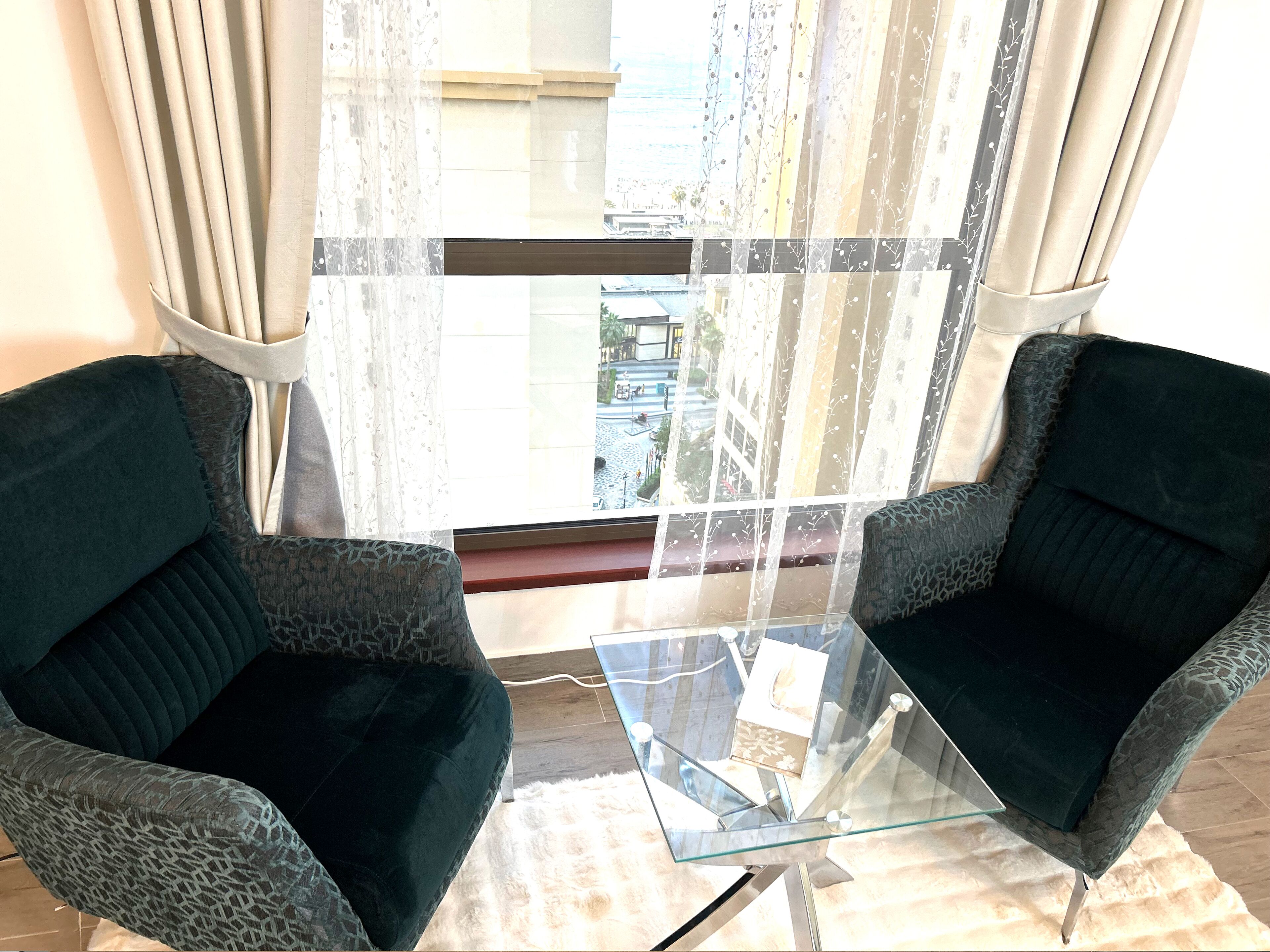 Une pièce comprenant deux fauteuils à motifs vert foncé, placés face à une table basse en verre.
