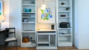 Una estantería blanca con varios objetos, entre ellos una máquina de escribir, adornos decorativos y un cuadro enmarcado.