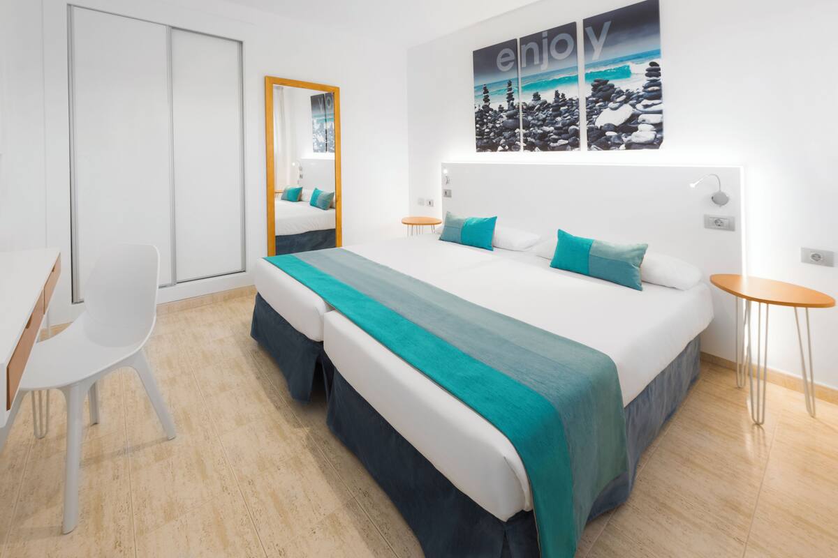 A modern hotel room with a large bed, two bedside tables, a chair, and a mirror.