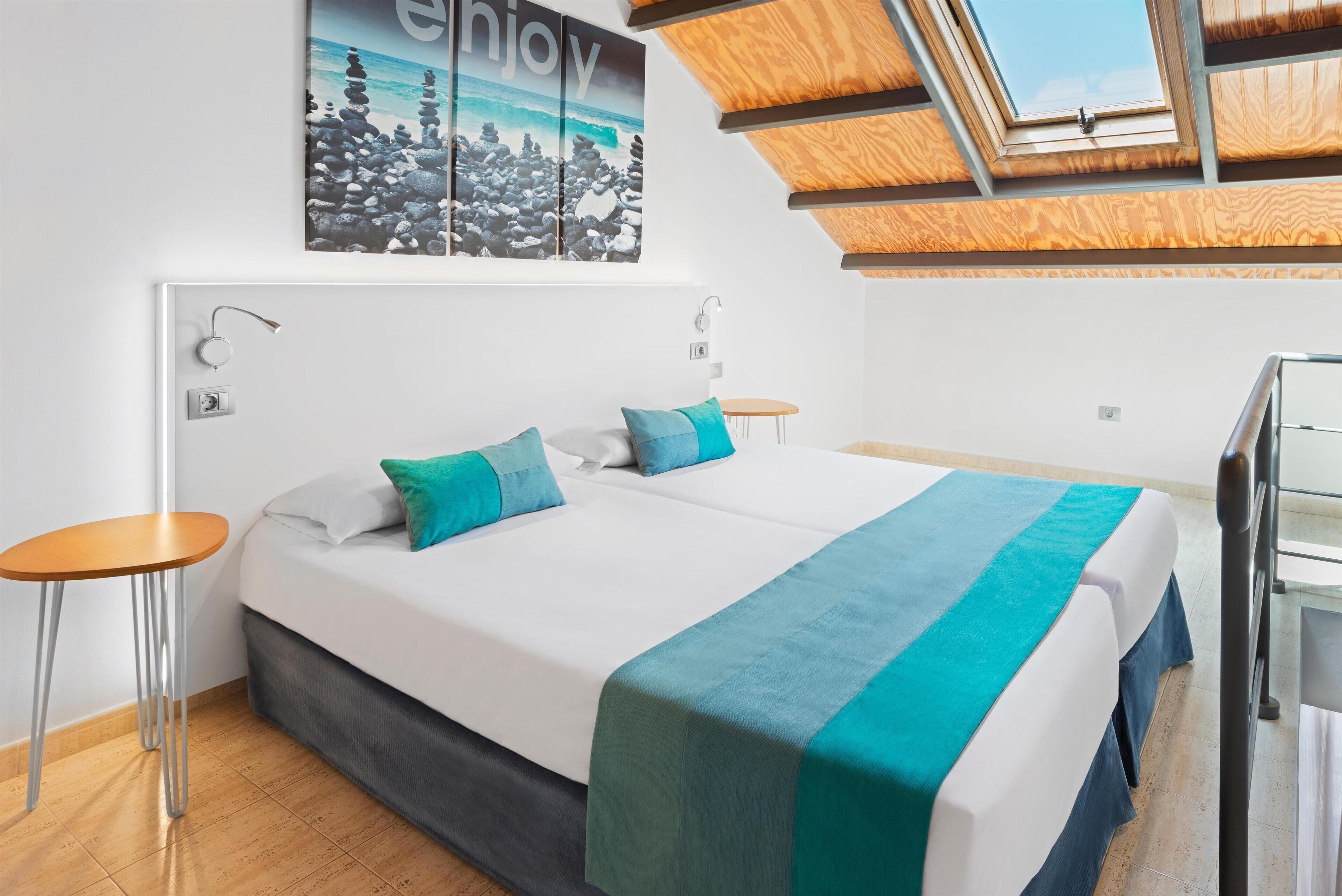 Ein modernes Hotelzimmer mit einem großen Bett, zwei Nachttischen, einem Oberlicht und Blick auf den Ozean.