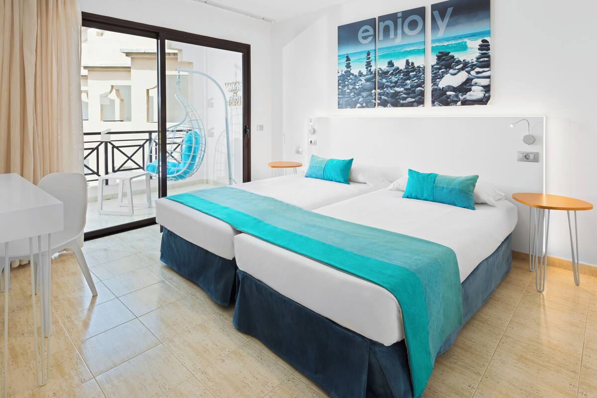A hotel room with a bed, two bedside tables, a chair, a balcony with a hanging chair, and a view of the sea.