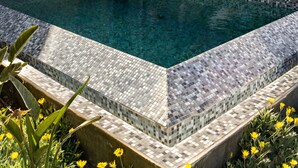 Un espace piscine extérieur moderne, agrémenté d’un mur en pierre et de deux chaises longues.